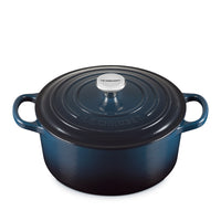 Pentola ovale in ghisa smaltata blu scuro con coperchio e manici laterali, pomello in acciaio con scritta Le Creuset, sfondo bianco