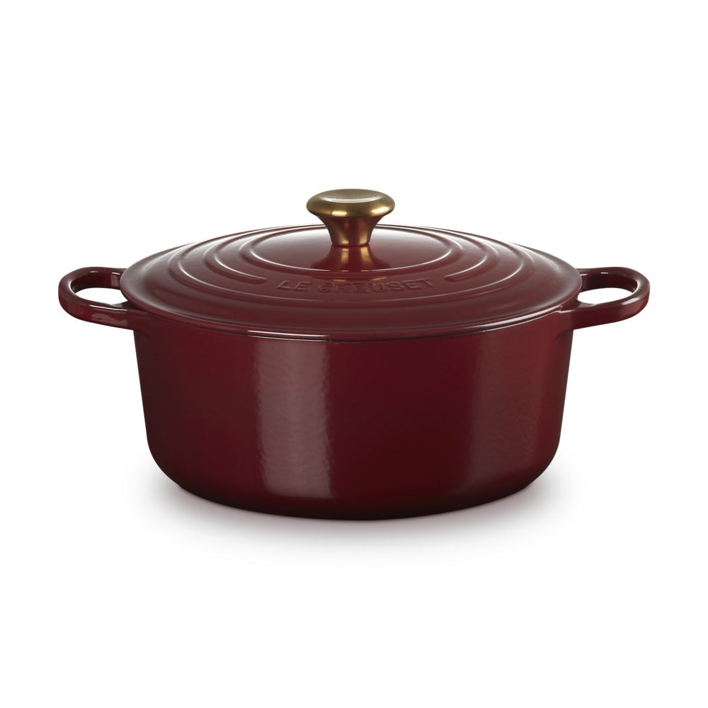 Casseruola rotonda in ghisa smaltata di colore rosso con coperchio e manico dorato, su sfondo neutro.