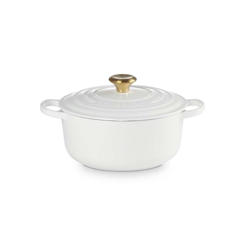 White cast iron casserole with lid, golden handle, smooth round surface, placed on a neutral background.