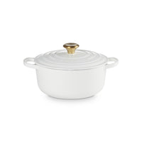 White cast iron casserole with lid, golden handle, smooth round surface, placed on a neutral background.