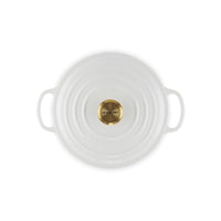 White ceramic saucepan with handles, central golden metal lid and engraved "LE CREUSET" lettering.