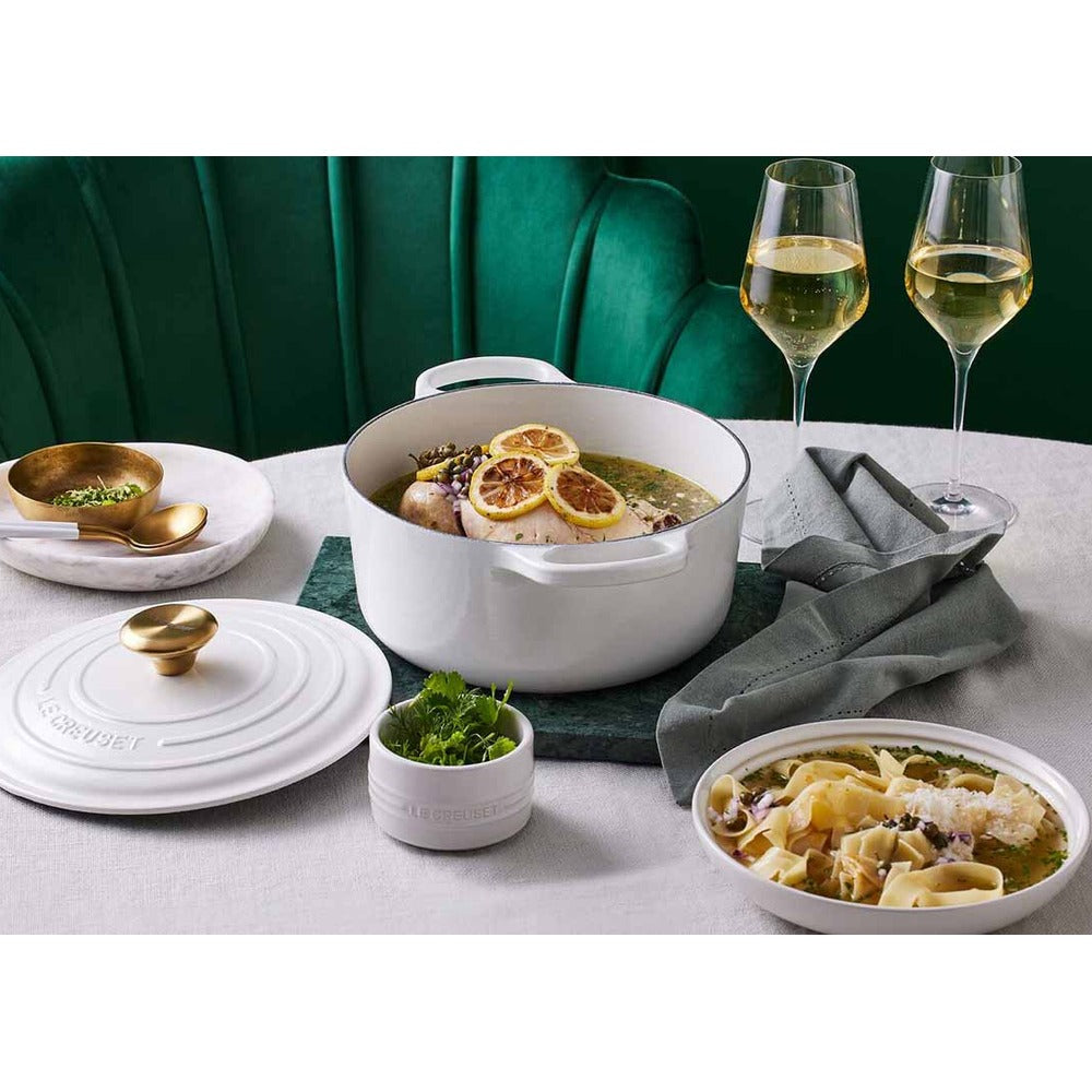 White pot with lid, pasta plate, wine glasses, gray tablecloth and green background. Gold decorations in containers.