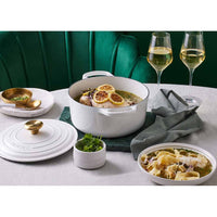 White pot with lid, pasta plate, wine glasses, gray tablecloth and green background. Gold decorations in containers.
