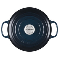 round dark blue enamelled cast iron lid with side handles and central metal knob with Le Creuset lettering, on white background