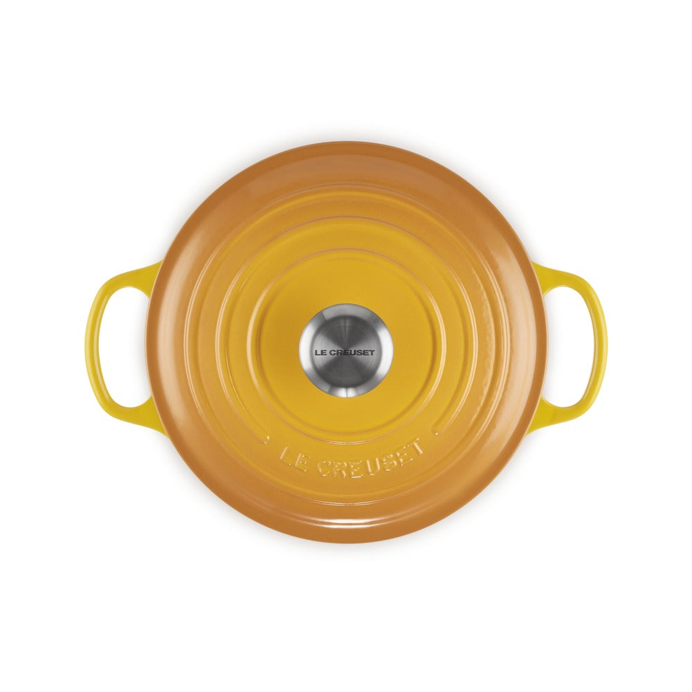 Round kitchen pot in warm yellow color with side handles, shiny finish and a lid with LE CREUSET logo in the center.