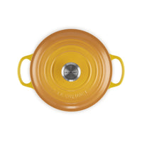 Round kitchen pot in warm yellow color with side handles, shiny finish and a lid with LE CREUSET logo in the center.