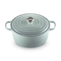 Light green saucepan with lid, side handles and metal knob. Embossed "LE CREUSET" logo.