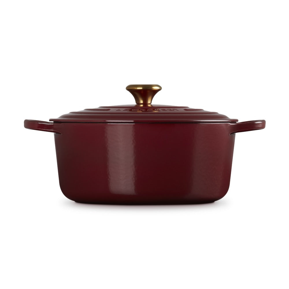 Casserole red in enamelled cast iron with lid and golden handle, placed on uno neutral background.