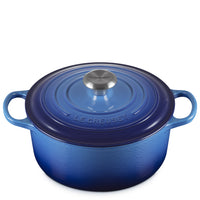 Blauwe geëmailleerde gietijzeren pan met deksel, zijhandgrepen en centrale metalen knop met opschrift Le Creuset, witte achtergrond