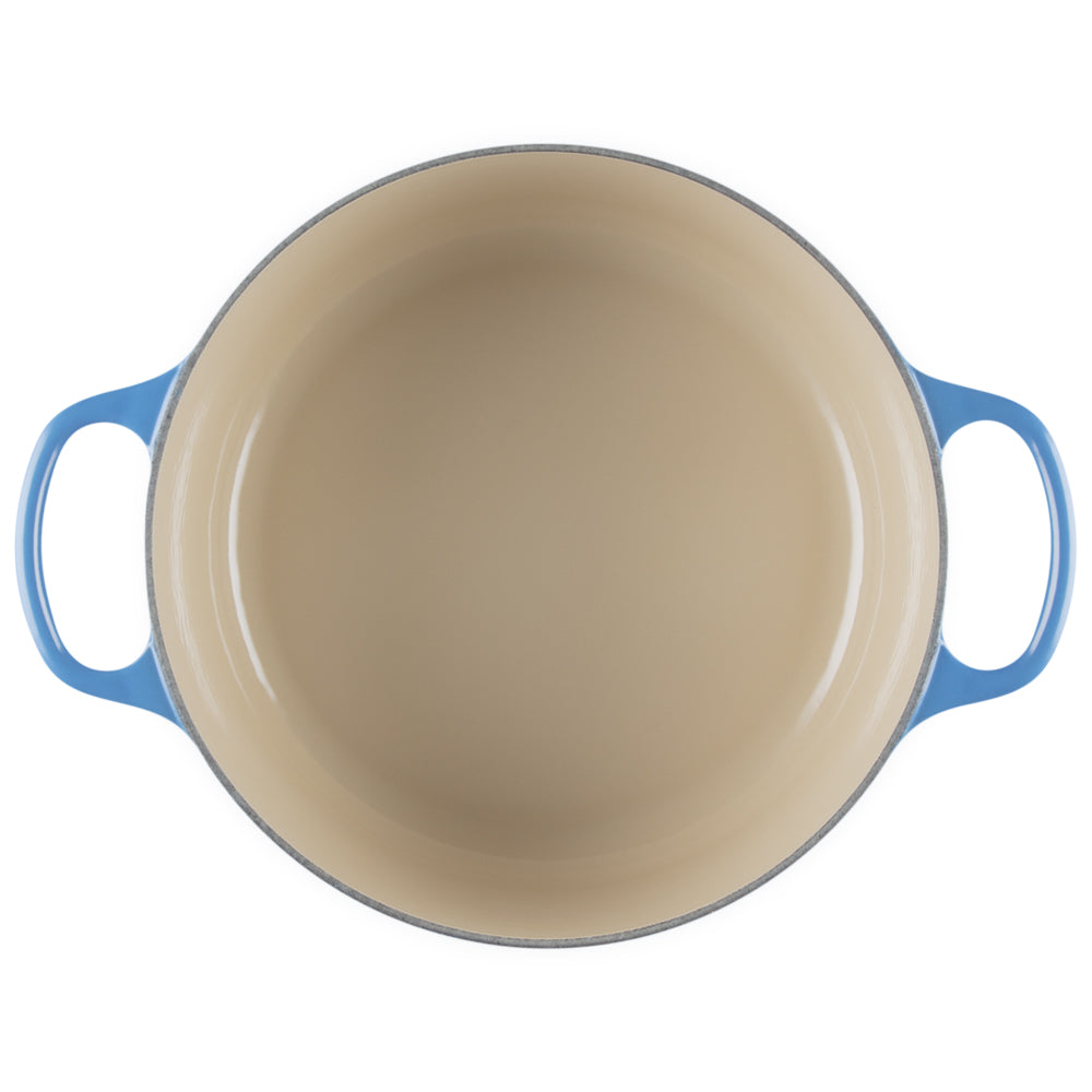 Ronde gietijzeren pan met beige binnenbekleding en blauwe buitenhandgrepen op witte achtergrond