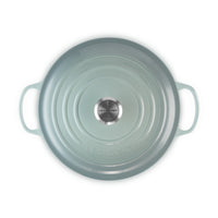 Ronde braadpan van keramiek lichtblauw, met twee handgrepen, logo "LE CREUSET" al centro, glanzend oppervlak en glad.