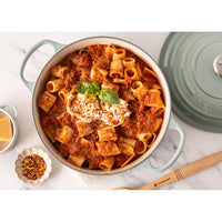 Rigatoni pasta with meat sauce, garnished with basil and cheese, in a light ceramic pot, on marble background.