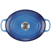 Couvercle ovale en fonte émaillée bleue avec poignées intégrées et pomme en acier avec inscription Le Creuset, fond blanc.
