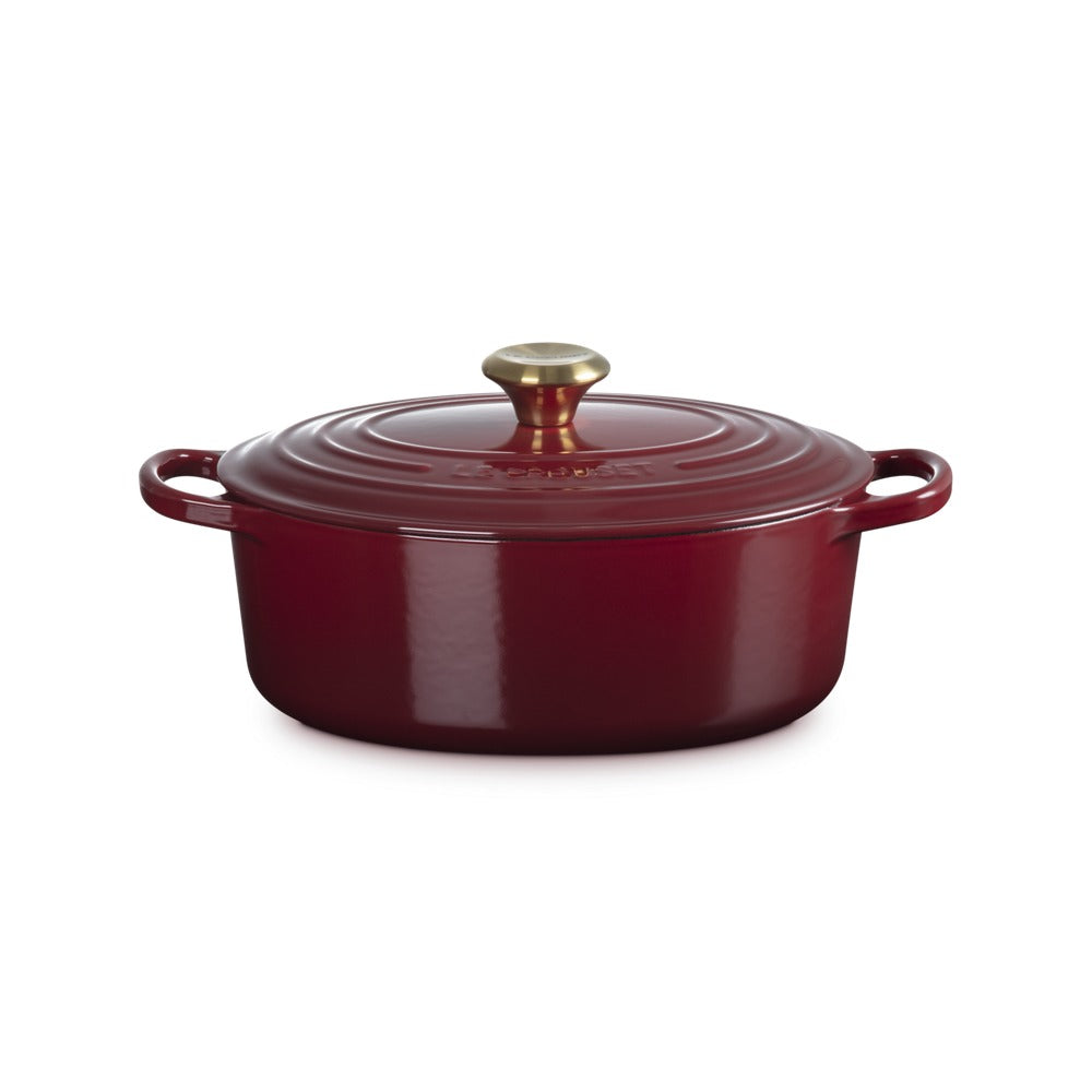 Casserole ovale de céramique rouge avec couvercle, anses latérales et bouton dorato.