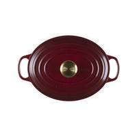 Assiette ovale rouge en fonte avec deux poignées et logo doré détaillé au centre, surface lisse et formes ondulées.
