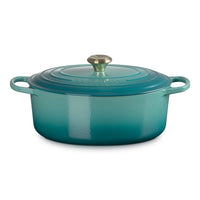 ovaal braadpan van geëmailleerd gietijzer, turquoise kleur, met deksel en gouden handgreep, op neutrale achtergrond.