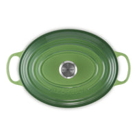 Groene ovale ovenschaal met handvatten, keramiekcoating, met roestvrijstalen bodem met "LE CREUSET"-logo.