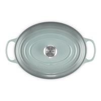 Aquagroene ovale ovenschaal met handgrepen, glanzende afwerking en centraal roestvrijstalen "LE CREUSET"-logo.