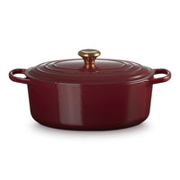 Ronde braadpan van geëmailleerd gietijzer rood, met deksel en gouden handgreep, op witte achtergrond.