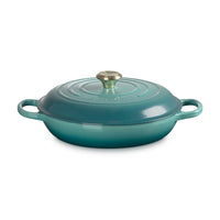 Casseruola rotonda di ceramica verde acqua, con coperchio, manici laterali e pomolo centrale dorato.
