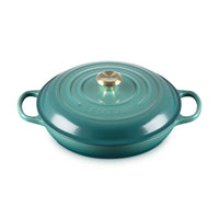 Casseruola ovale in ceramica smaltata verde acqua, con coperchio e manico dorato, superficie liscia e lucida.