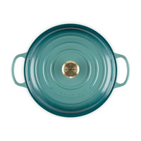 Pentola rotonda in ghisa smaltata di colore verde acqua, con manici laterali e pomolo centrale oro.
