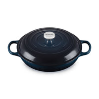 Casseruola rotonda in ghisa smaltata blu scuro con coperchio e due manici laterali.