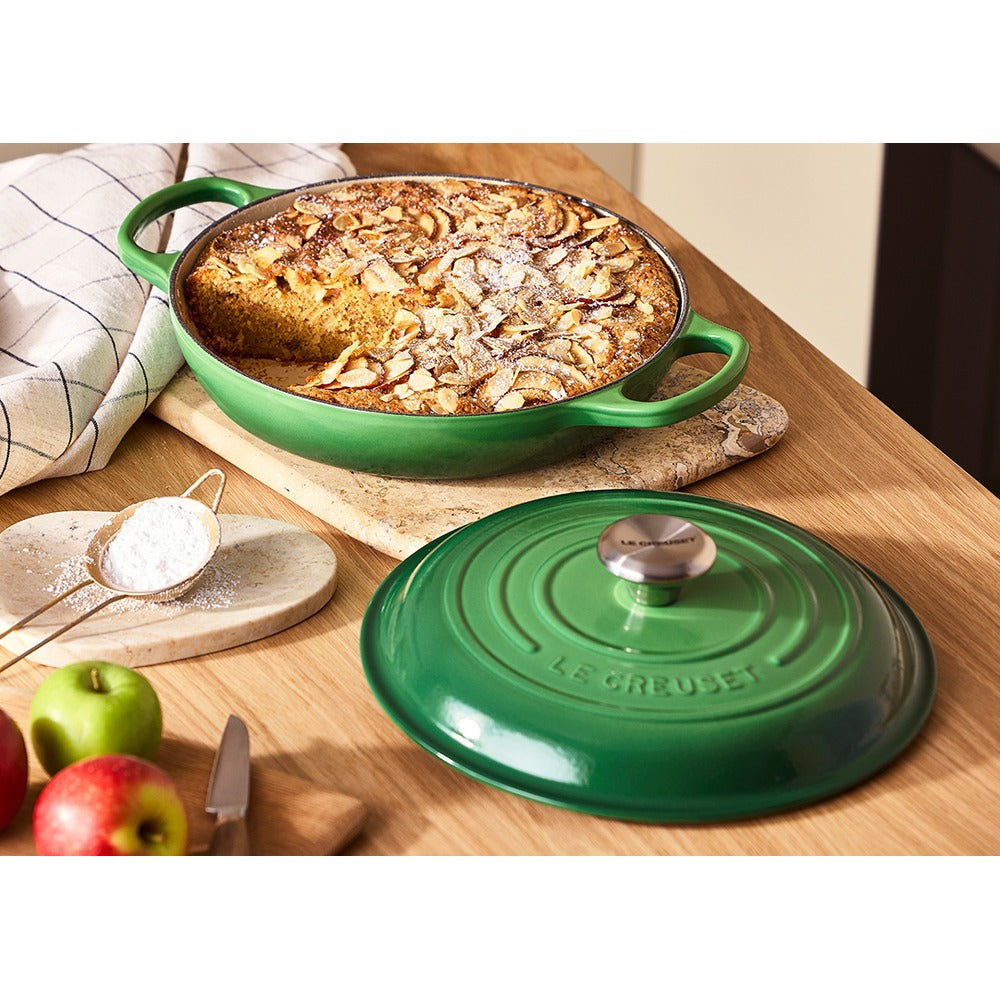 Teglia verde di ceramica con dolce alle mele, guarnito con mandorle e zucchero a velo, circondata da mele e una ciotola di zucchero.