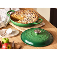 Teglia verde di ceramica con dolce alle mele, guarnito con mandorle e zucchero a velo, circondata da mele e una ciotola di zucchero.