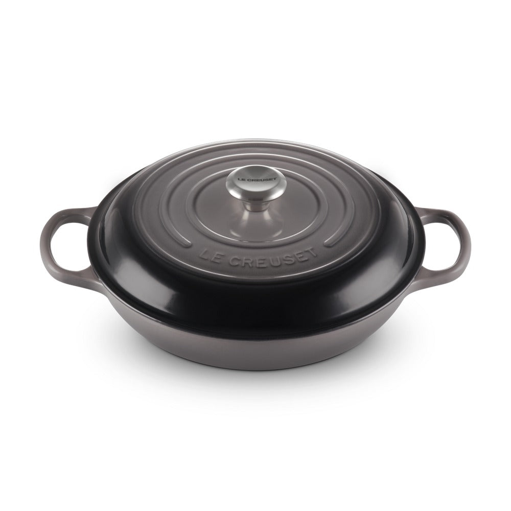 Casseruola ovale in ghisa smaltata nera con coperchio, manici laterali, marchio "LE CREUSET" inciso. Sfondo neutro.