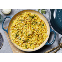 Pasta linguine con sugo giallo, guarnita con prezzemolo e formaggio grattugiato, servita in una casseruola blu.