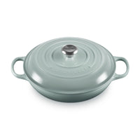 Casseruola ovale verde acqua con coperchio in metallo e manici, superficie lucida, con il logo "LE CREUSET" ben visibile.