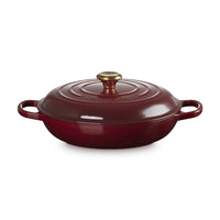 Casseruola rotonda in ghisa smaltata rossa con coperchio e manico dorato, posizionata su sfondo bianco.
