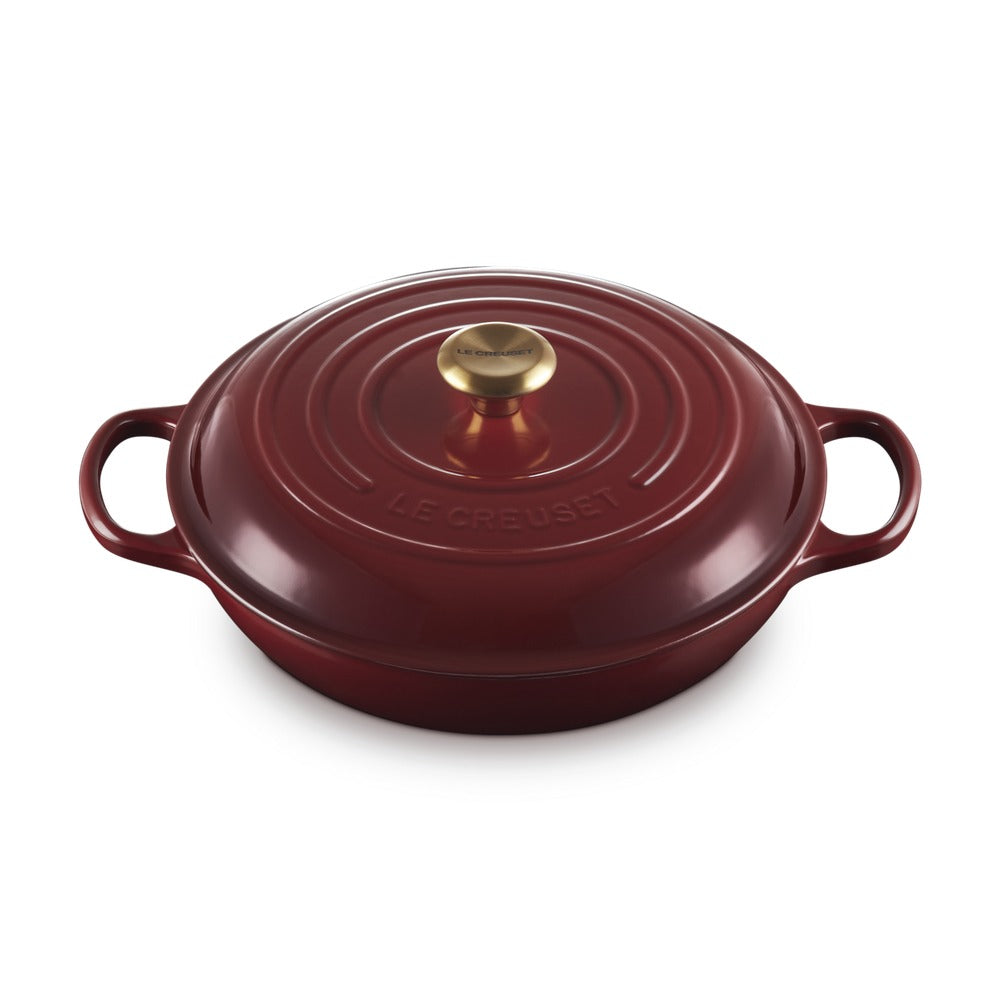 Casseruola rotonda in smalto rosso, con coperchio e manico dorato, su sfondo neutro.
