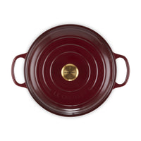 Casseruola rotonda di colore bordeaux con manici e fondo in metallo dorato, marchiata "LE CREUSET".