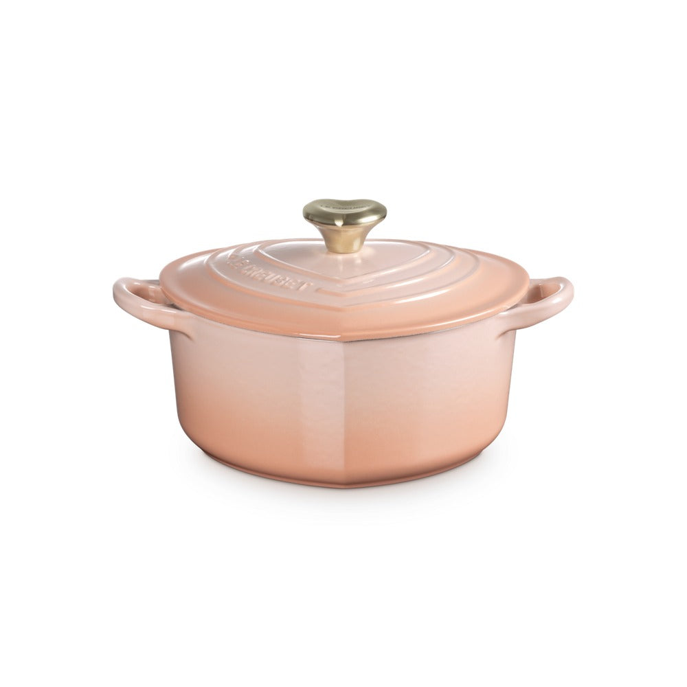 Olla de cerámica rosa con tapa, mango dorado y detalles ondulados, sobre fondo neutro.