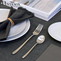 Satin-finish steel cutlery with fork and teaspoon on napkin and white plates with dark grey decoration
