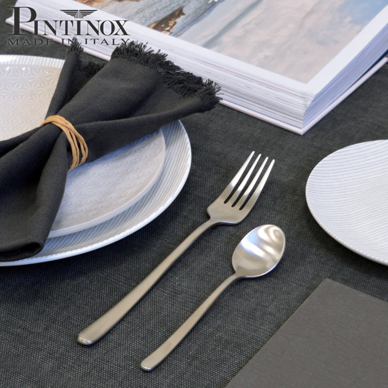 Satin-finish steel cutlery with fork and teaspoon on napkin and white plates with dark grey decoration