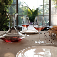 Karaf en twee transparante wijnglazen met roséwijn, glas versierd met rode stippen, witte borden op gedekte tafel in