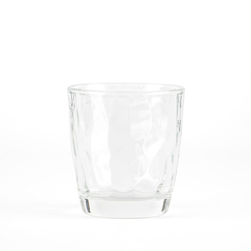 Transparent glass tumbler with wavy surface, resting on white background.