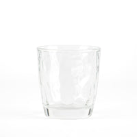 Transparent glass tumbler with wavy surface, resting on white background.