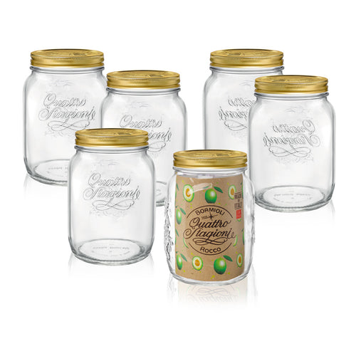 Sechs transparente Glasgefäße mit goldenem Deckel, eines mit braunem Etikett mit grünen Oliven und erhabener "Quattro Stagioni" Schrift.