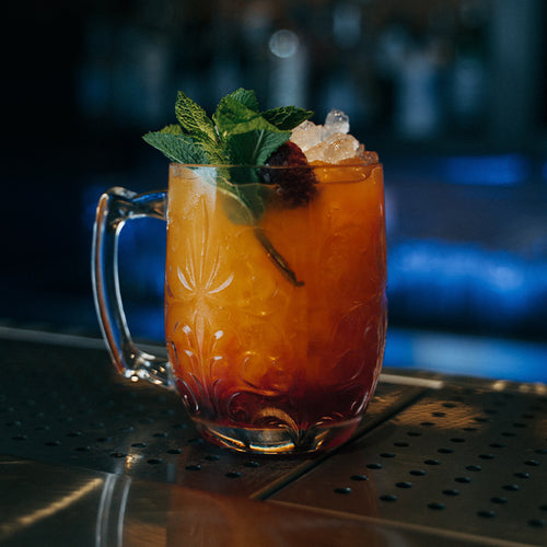 Engraved Glasbecher mit hundle mit orange Cocktail mit crushed Eis, mint leaves und raspberry, auf metal counter.