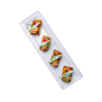 Quattro tartine triangolari con salmone, aneto, spicchi di mela e chicchi di melograno su piatto bianco