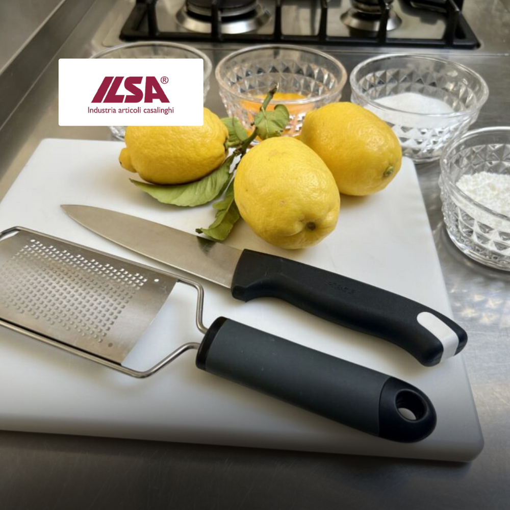 tre limoni gialli con foglie, coltello e grattugia in metallo e plastica nera, su tagliere bianco in cucina