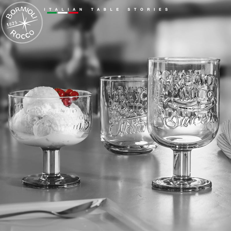 Set de verres et coupe en verre transparent avec décorations en relief, un avec glace et cerises sur table.