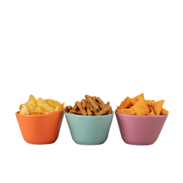Tre ciotole colorate in ceramica arancione, azzurra e rosa con patatine fritte, snack salati e bastoncini