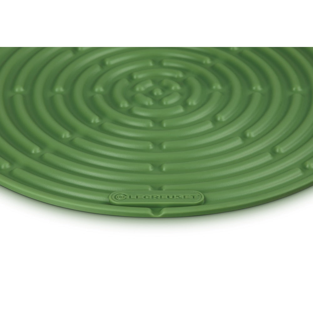 Tapis circulaire vert à motif spiralé, en silicone, logo Le Creuset visible. Fond blanc.
