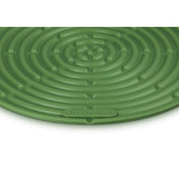 Tapis circulaire vert à motif spiralé, en silicone, logo Le Creuset visible. Fond blanc.