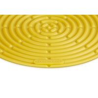 Tapis circulaire jaune en silicone à motif spiralé, portant la marque "Le Creuset" en relief.